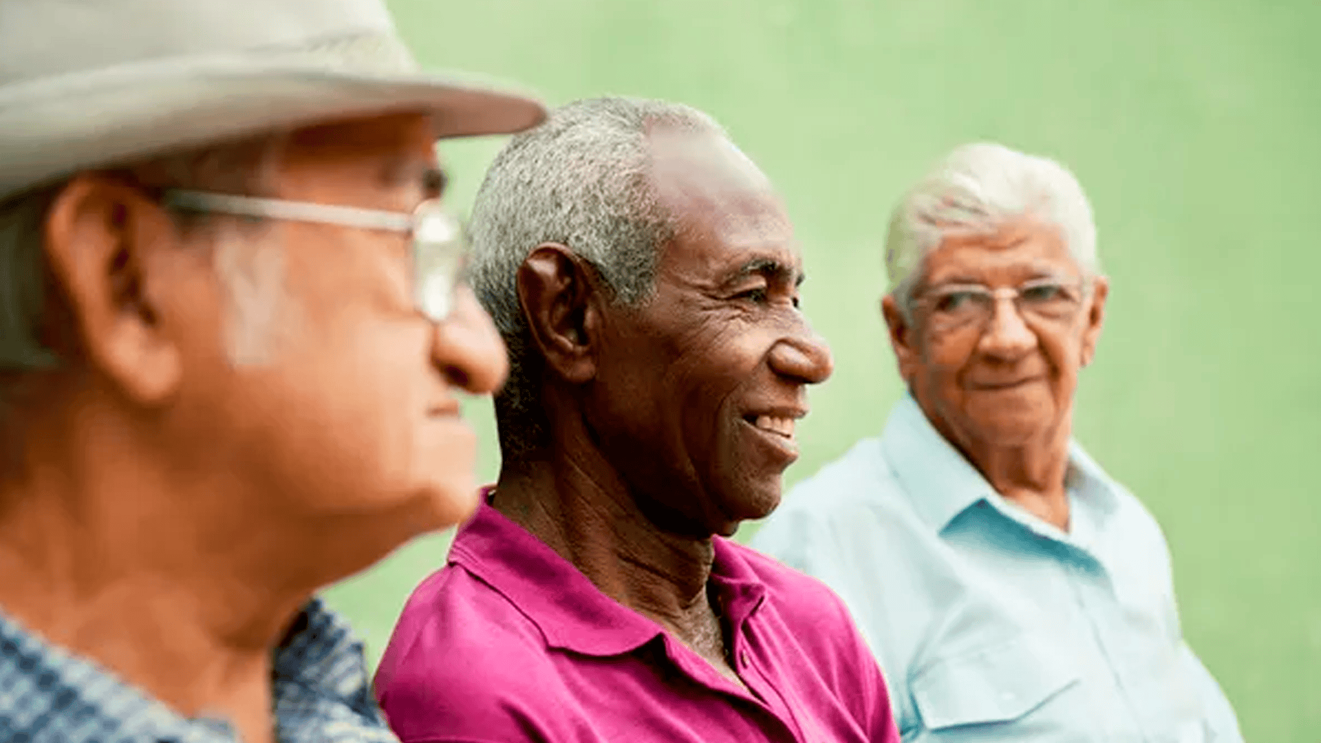 3 senhores idosos conversando e sorrindo. Provavelmente em um banco de praça.