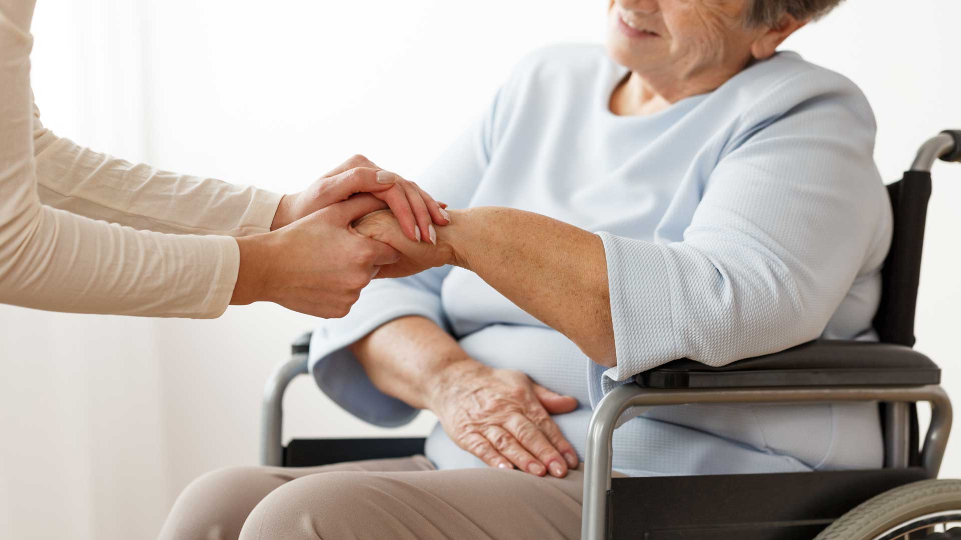 Uma senhora na cadeira de rodas recebendo atenção de uma médica que segura suas mãso em sinal de carinho